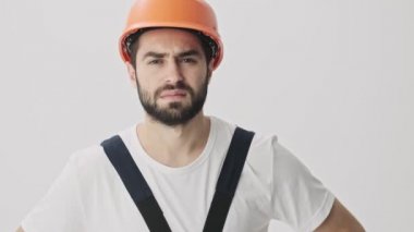 Hoşnutsuz genç sakallı adam miğferiyle beyaz duvar arkasında izole edilmiş.