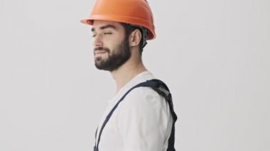 İyimser genç sakallı adam miğferiyle beyaz duvar arkasında izole edildi.