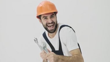 Mutlu, sakallı adam müteahhiti beyaz duvar arkasında ingiliz anahtarıyla dans ediyor.