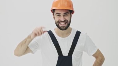 Mutlu, genç, sakallı adam miğferiyle beyaz duvar arkasında izole edilmiş.