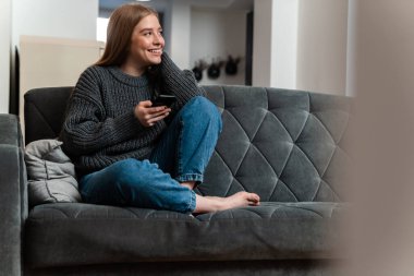 Evde cep telefonu kullanan memnun bir genç kadının görüntüsü.