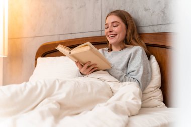 Evde, evde kitap okuyan mutlu, genç bir kadının fotoğrafı..