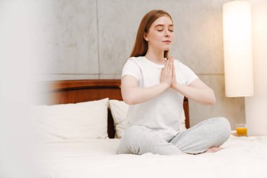 Evde, yatak odasında, yatakta meditasyon yapan tatlı bir kız resmi..