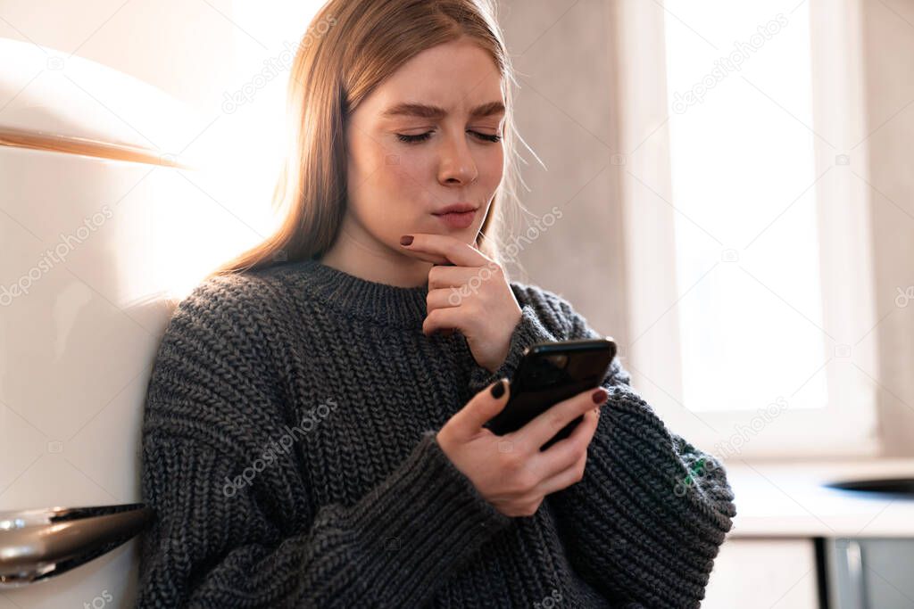Image of a concentrated serious amazing young woman indoors at home using mobile phone.