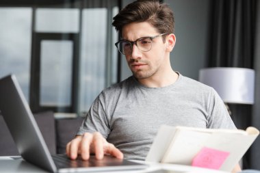 Evde dizüstü bilgisayarla doküman tutan yakışıklı bir gencin resmi..