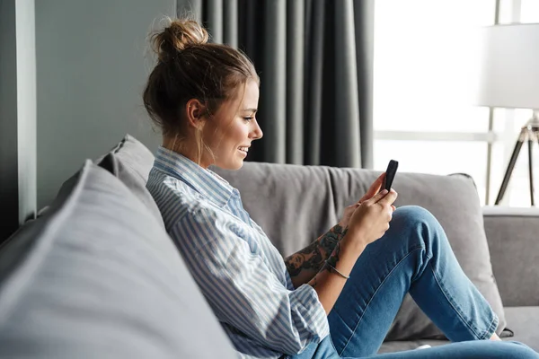 Çizgili Tişörtlü Mutlu Genç Bir Kadının Oturma Odasında Koltukta Otururken — Stok fotoğraf