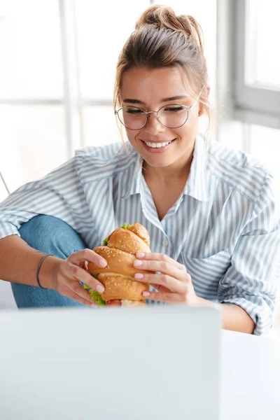 Smiling young businesswoman having lunch while working on laptop computer at home