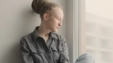 Rasta saçı olan konsantre bir kız pencerenin yanında oturuyor.
