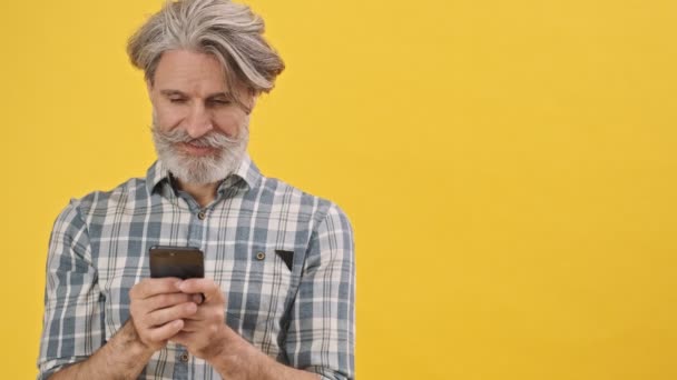 用手机聊天隔离在黄色背景下的令人惊讶的老人 — 图库视频影像