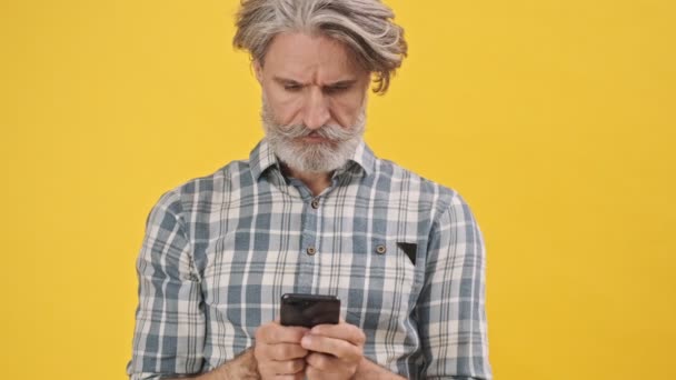 Homem Idoso Confuso Isolado Sobre Fundo Amarelo Usando Telefone Celular — Vídeo de Stock
