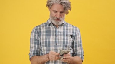 Kıdemli yakışıklı adam sarı arka planda izole edilmiş. Sana para veriyor.