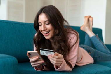 Evde koltukta cep telefonu kullanan iyimser bir genç kadın görüntüsü..