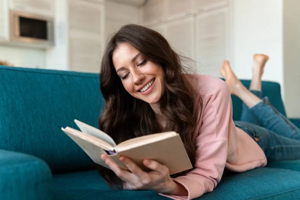 Obraz Uśmiechniętej Młodej Kobiety Domu Czytającej Książkę Leży Kanapie — Zdjęcie stockowe