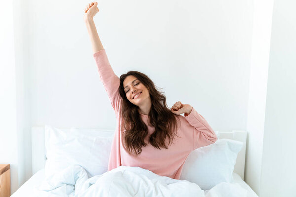 Image of a pretty young woman indoors at home lies in bedroom in bed stretching.