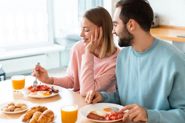 若い幸せなカップルの肖像画自宅で居心地の良いキッチンで朝食を食べながらテーブルで一緒に食べる — ストック写真