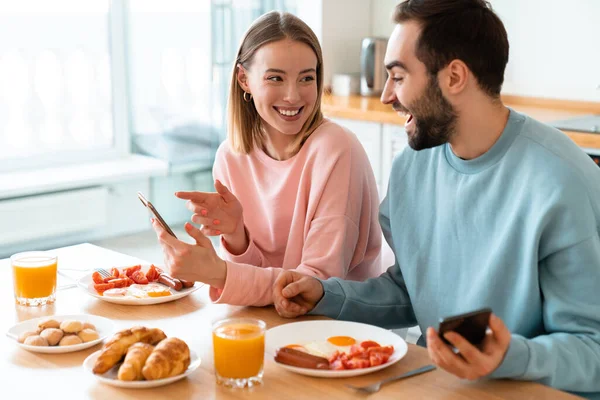 Portrait Young Joyful Couple Using Cellphones Laughing While Having Breakfast — Stock Photo, Image