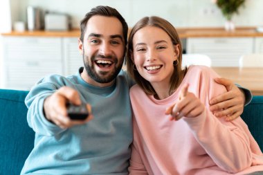 Evdeki rahat odada kanepede otururken sarılıp televizyon izleyen genç çiftin portresi.