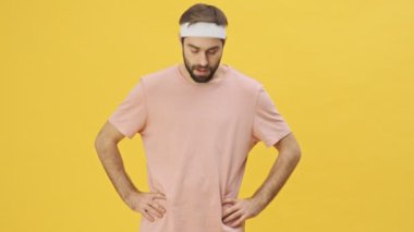 Spor giyim sektöründe genç ve çekici bir adam spor yapıyor. Başını hareket ettiriyor ve boynunu uzatıyor. Stüdyoda sarı bir arka planda izole bir şekilde.
