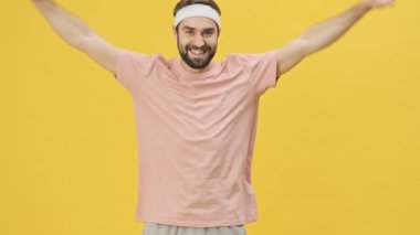 Spor giyimli mutlu ve enerjik genç bir sporcu stüdyoda sarı bir arka planda izole edilmiş egzersizler yapıyor.