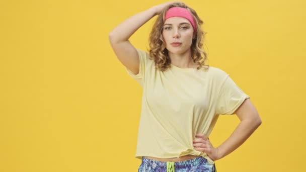 一位身穿运动服的年轻漂亮的女运动员正在演播室里 在一个黄色的背景下独立进行体育锻炼 休息片刻 — 图库视频影像