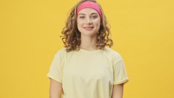 スポーツウェアの美しい若い運動選手がスタジオで黄色の背景の上に隔離された笑顔 — ストック動画