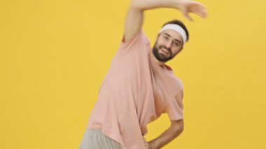 Spor giyimli yakışıklı genç bir sporcu stüdyoda sarı bir arka planda izole edilmiş egzersizler yapıyor.