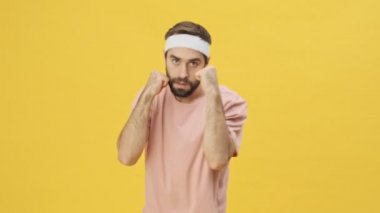 Spor giyim sektöründe yakışıklı genç bir sporcu boks antrenmanı yapıyor. Sonra sarı arka planda izole edilmiş bir jest yapıyor.