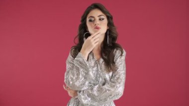 Parlak pullu bir elbise giyen düşünceli genç bir kadın pembe duvar arkasında izole edilmiş iyi bir fikirle geliyor.