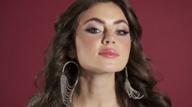 Parlak pullu elbise giymiş güzel bir kadın, pembe duvar arkasında izole edilmiş aynaya bakar gibi kameraya bakıyor.