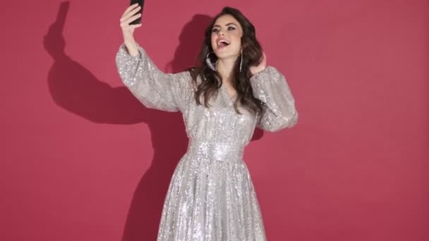 明るいスパンコールドレスの魅力的な感情的な若い女性はピンクの壁の背景に隔離された写真を撮っています — ストック動画