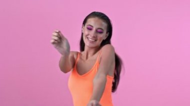 Pembe duvar arkasında dans eden harika, mutlu, pozitif bir kadın.