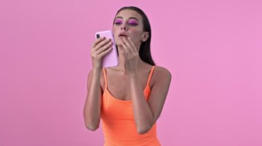 Pembe duvarın üzerinden izole edilmiş, cep telefonuna bakan genç bir kadın.