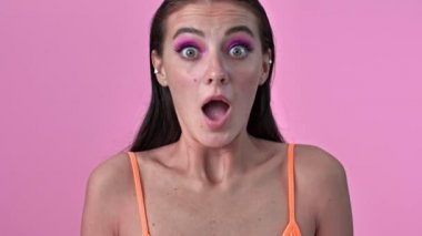 Genç, kafası karışmış, pembe duvarın üzerinde izole bir kadın.