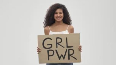 Genç Afrikalı mutlu, pozitif, harika bir kadın beyaz duvar arkasında yalnız poz veriyor feminist metinlerle boş duruyor.