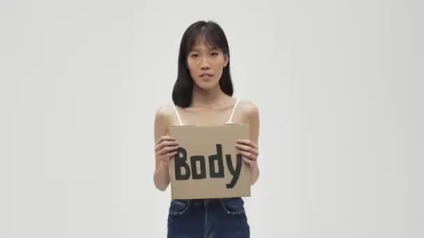 若いですアジアの可愛いです女性Posing隔離された上にホワイトウォール背景保持ブランクとともにフェミニストテキスト — ストック動画