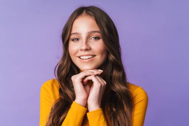 Uzun kahverengi saçlı, gülümseyen ve kameraya poz veren, menekşe arkaplanından izole genç ve güzel bir kadın.