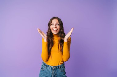 Uzun kahverengi saçlı, gülümseyen ve zevkle el kaldıran, menekşe arkaplanından soyutlanmış güzel bir kadın görüntüsü.