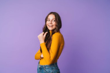 Uzun kahverengi saçlı, gülümseyen ve telif alanını gösteren güzel bir kadın resmi. Mor arka planda izole edilmiş.