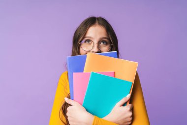 Gözlük takan genç ve güzel bir kız öğrencinin elinde menekşe arkaplanından izole edilmiş egzersiz kitapları.