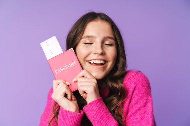 Uzun kahverengi saçlı, elinde pasaport ve seyahat bileti olan güzel bir kadının görüntüsü mor arka planda izole edilmiş.