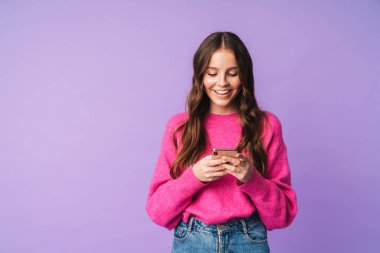 Güneş gözlüğü takan, gülümseyen ve cep telefonunu menekşe arka planda saklanmış güzel bir kadın görüntüsü.