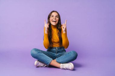 Bacakları çapraz oturan ve menekşe arkaplanda izole edilmiş telif uzayını gösteren güzel bir kadın resmi