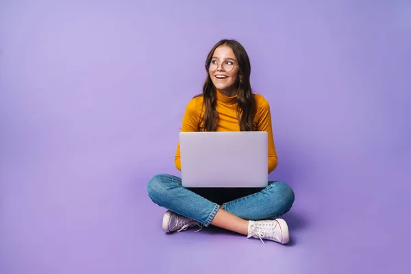 年轻而漂亮的女人坐在笔记本电脑上 双腿交叉在紫罗兰的背景上 — 图库照片