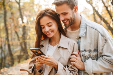 Güz parkında zaman geçirirken cep telefonu kullanan güzel bir çift.