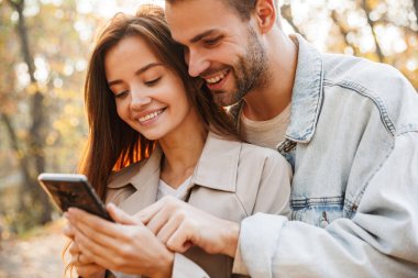 Güz parkında zaman geçirirken cep telefonu kullanan güzel bir çift.
