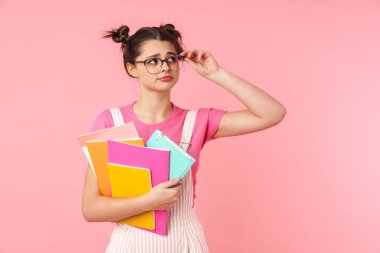 Güzel üzgün genç kız pembe arka planda tek başına duruyor, ders kitaplarını taşıyor.