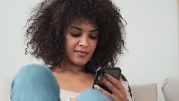 若い楽観的なアフリカの巻き女性屋内で自宅で使用して携帯電話 — ストック動画
