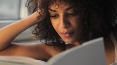Evde kitap okuyan güzel Afrikalı kıvırcık kadın.