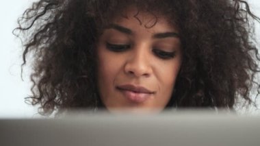 Evde dizüstü bilgisayar kullanan, genç, pozitif, Afro-Afrikalı kıvırcık kadın.