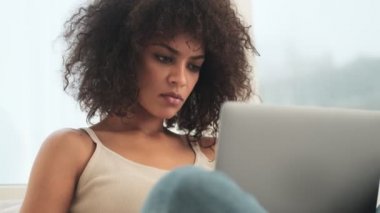 Genç konsantre olmuş Afrikalı kıvırcık kadın evde dizüstü bilgisayar kullanıyor.